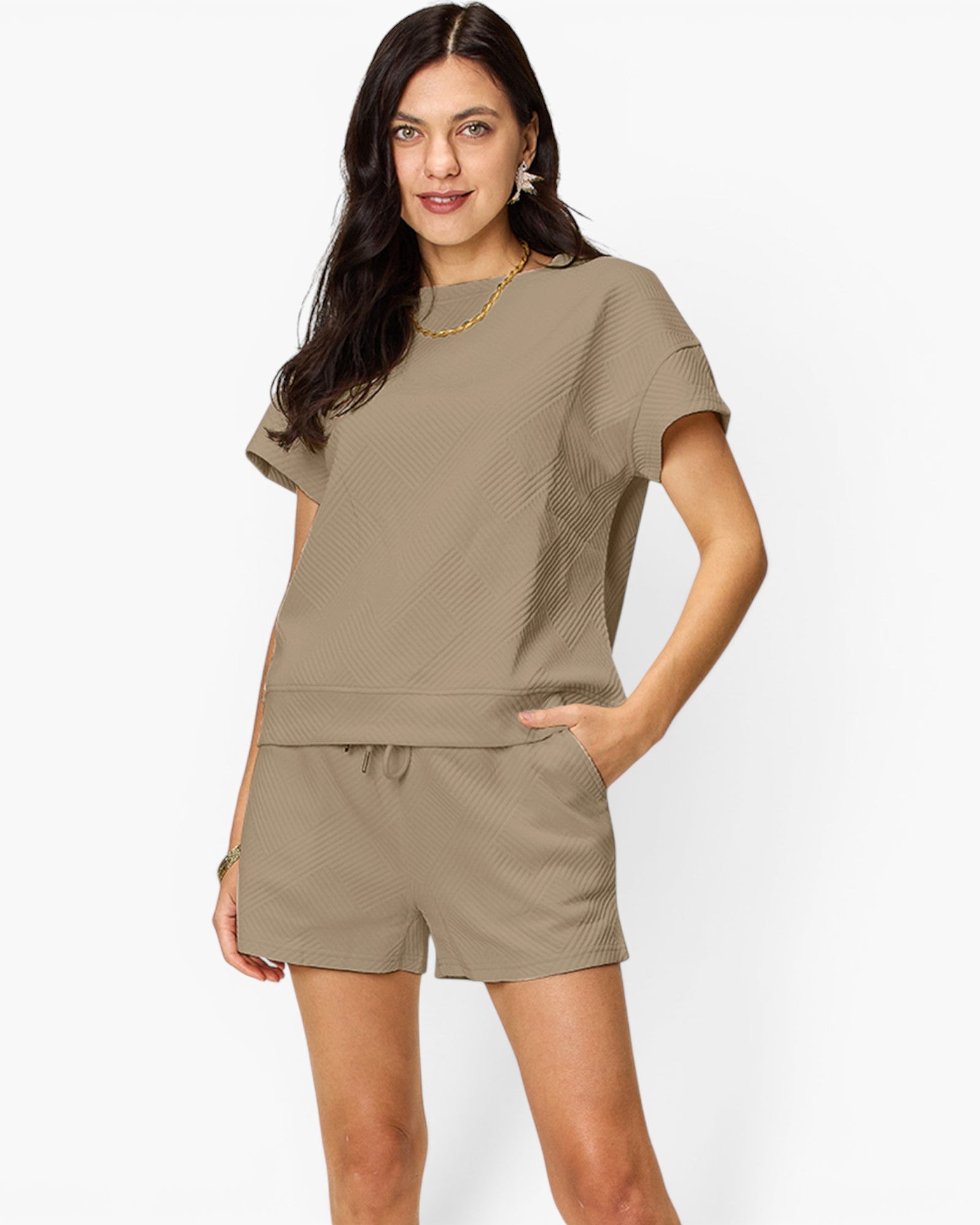 A woman modeling a matching two-piece lounge set in a textured taupe color, featuring a short-sleeve top and shorts with a drawstring waist, against a plain white studio background.