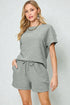 Woman wearing a gray outfit with shorts on a plain background