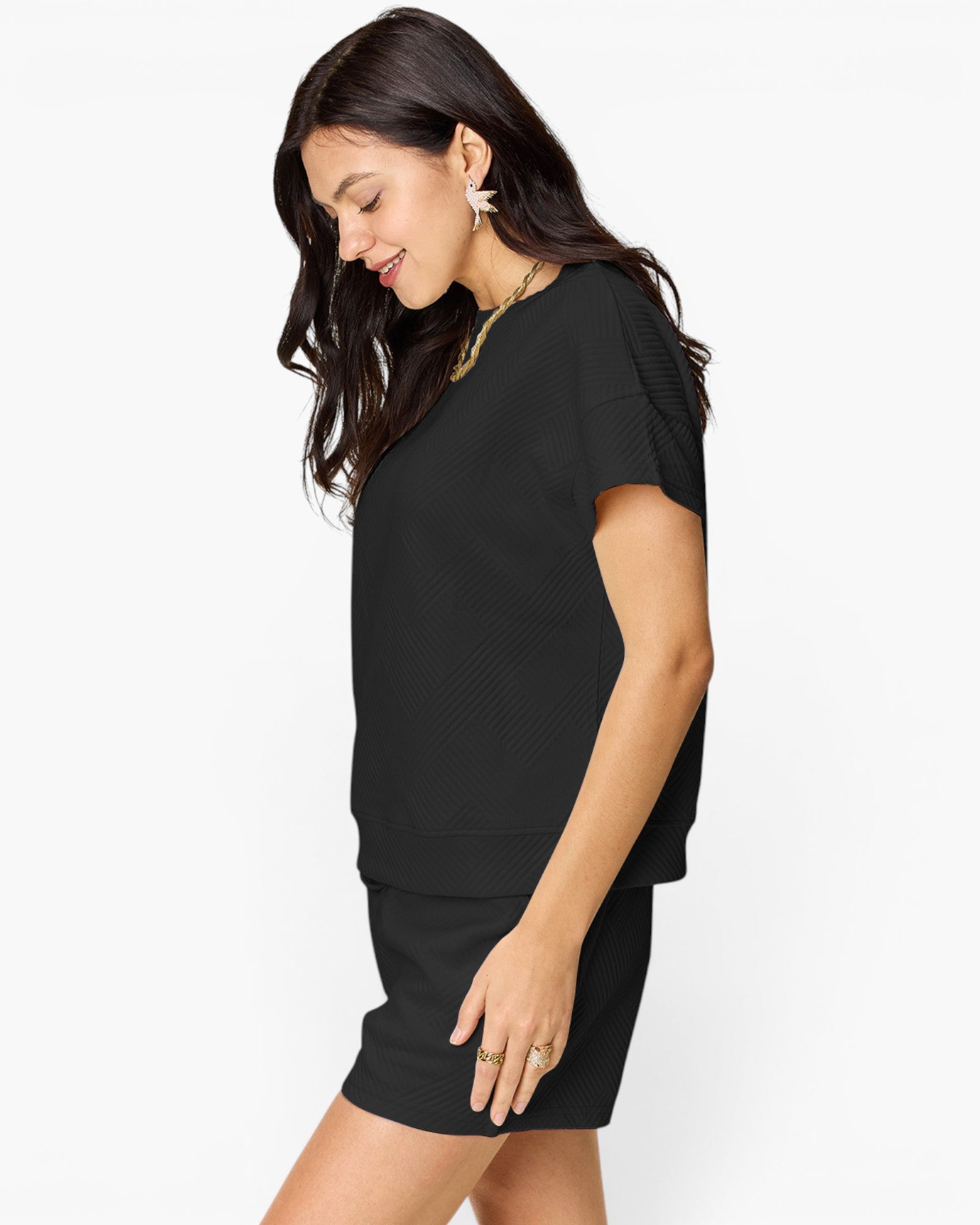 A woman wearing a black short-sleeve knit dress with textured side panels, shown from a side profile against a plain white studio background.