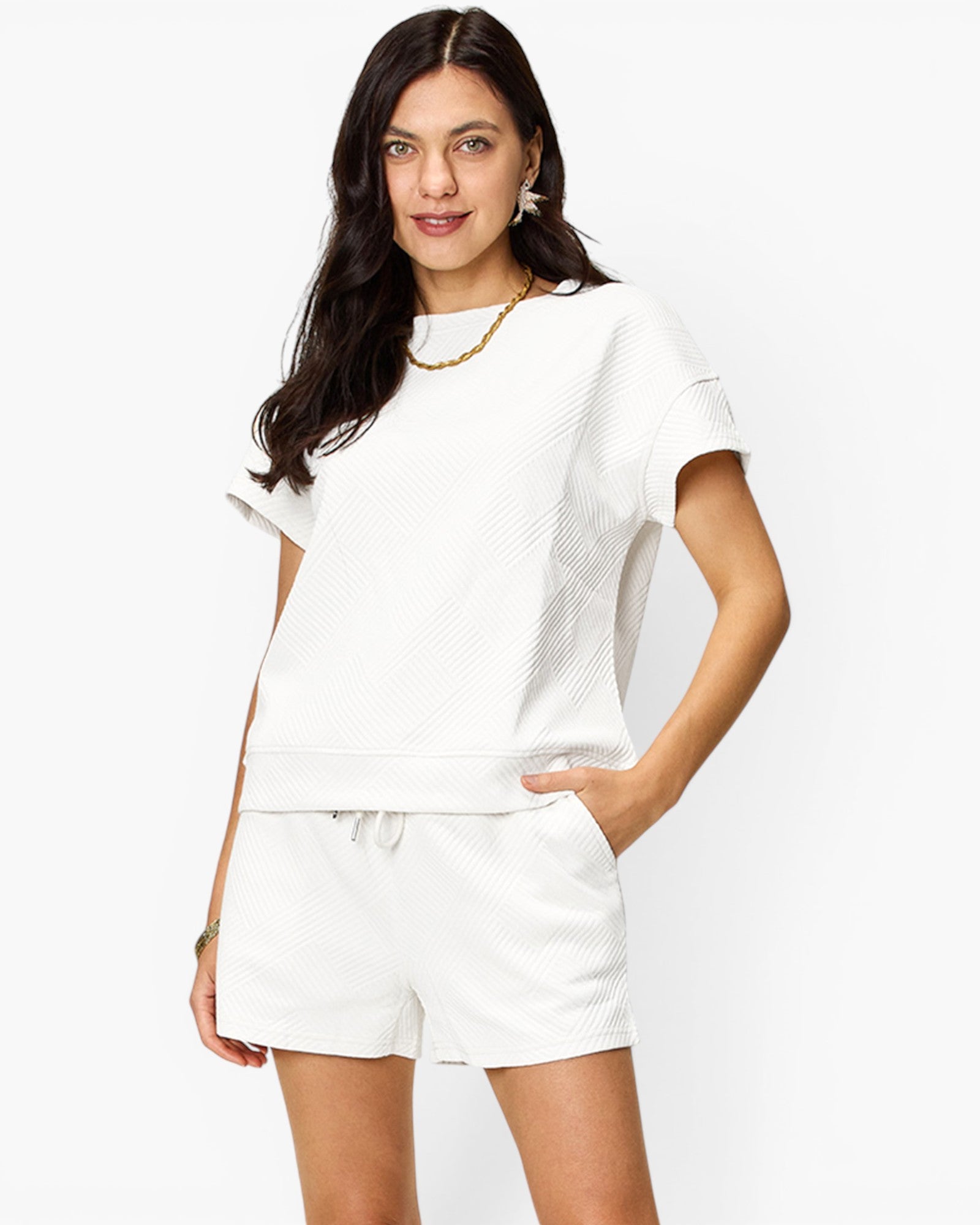 A woman modeling a white textured short-sleeve top and matching white shorts against a plain white studio background.