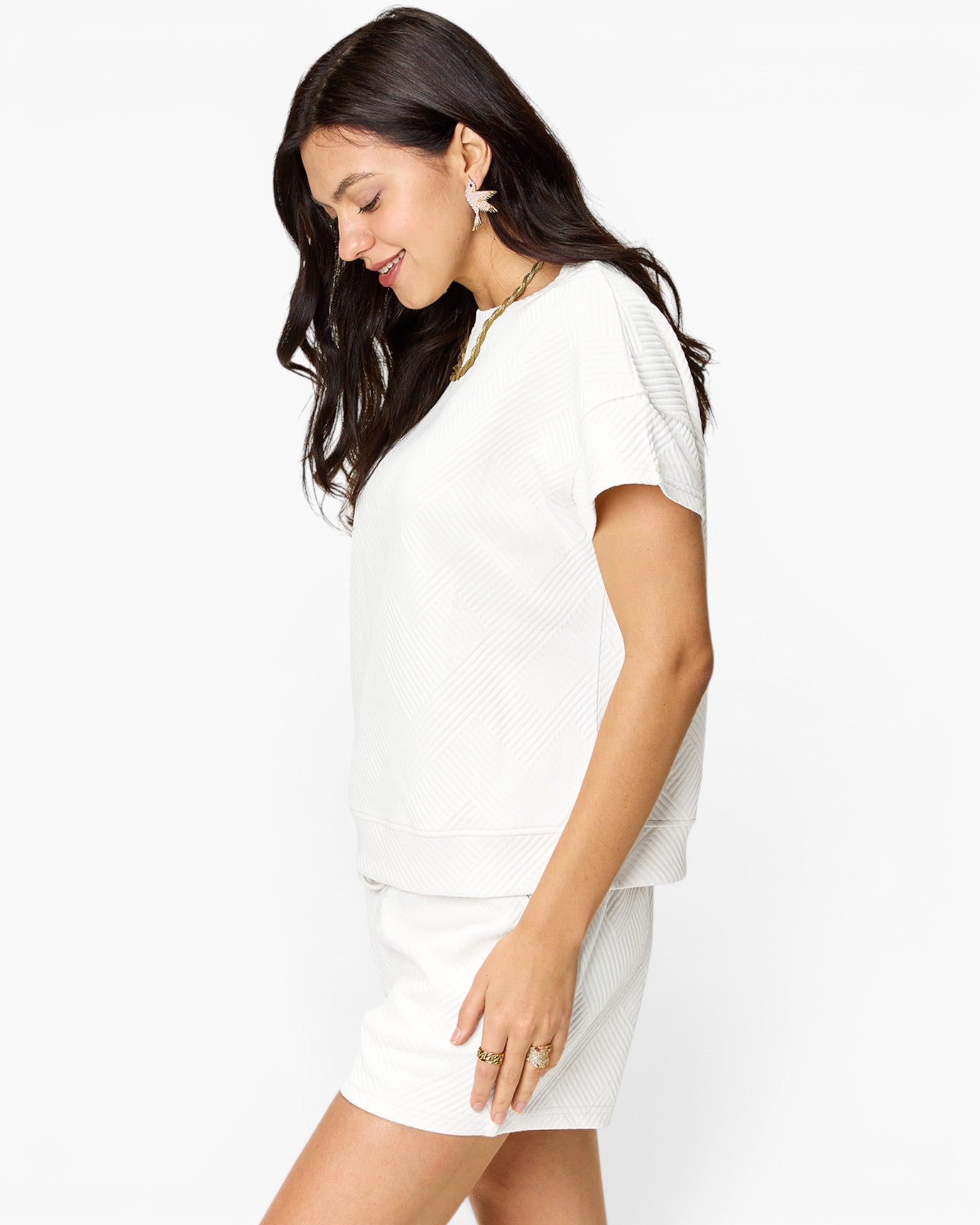 A woman wearing a white short-sleeve knit top and matching white shorts, photographed against a clean white studio background.