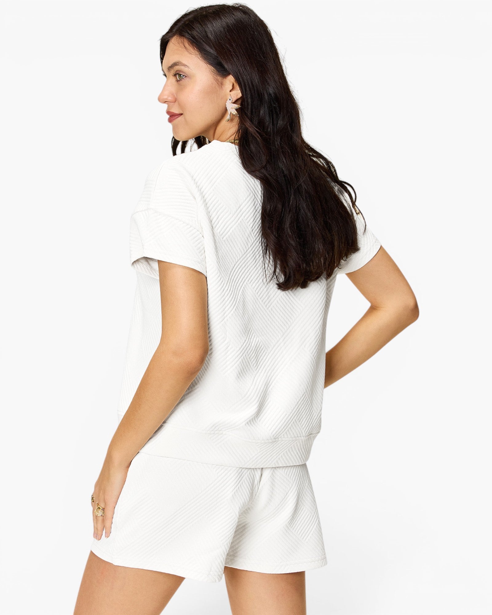 A woman wearing a matching white short-sleeve knit top and shorts set, shown from a three-quarters back view against a plain white studio background.