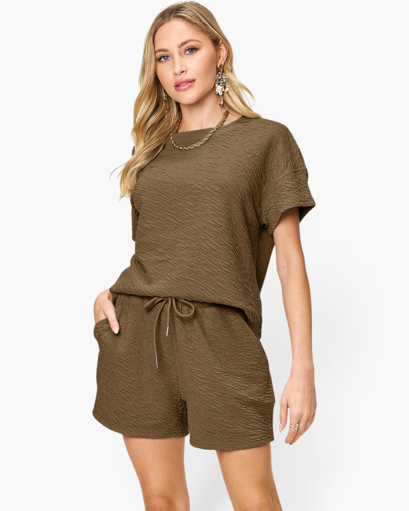 A woman modeling a matching two-piece lounge set in a textured olive-brown fabric, featuring a short-sleeve top and drawstring shorts, against a plain white background.