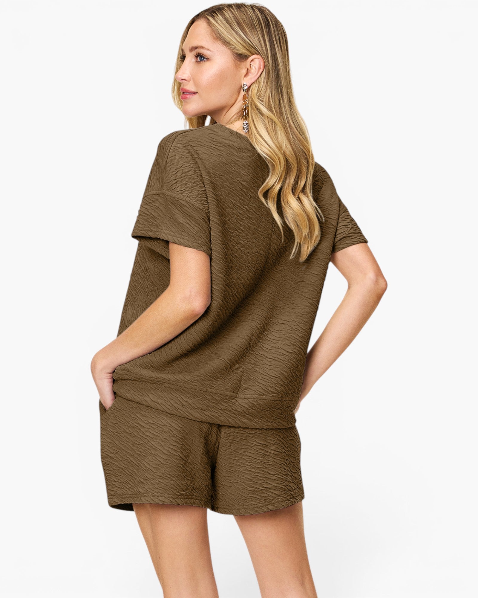 A woman modeling a matching short-sleeve top and shorts set in a textured olive brown fabric, shown from a three-quarters back view against a plain white background.