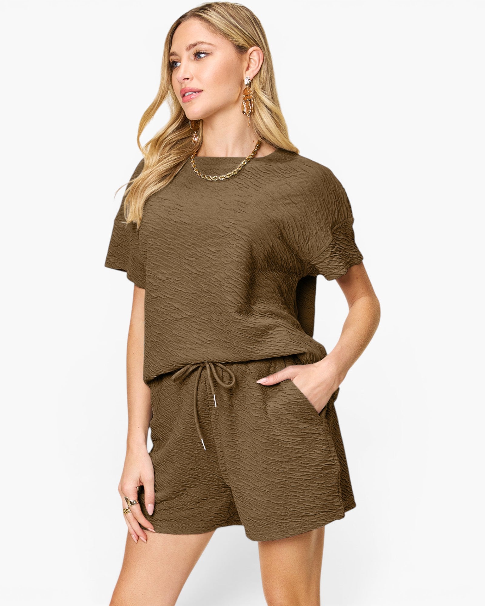 A woman modeling a matching two-piece lounge set in a textured olive-brown color, featuring a short-sleeve top and drawstring shorts, against a plain white background.
