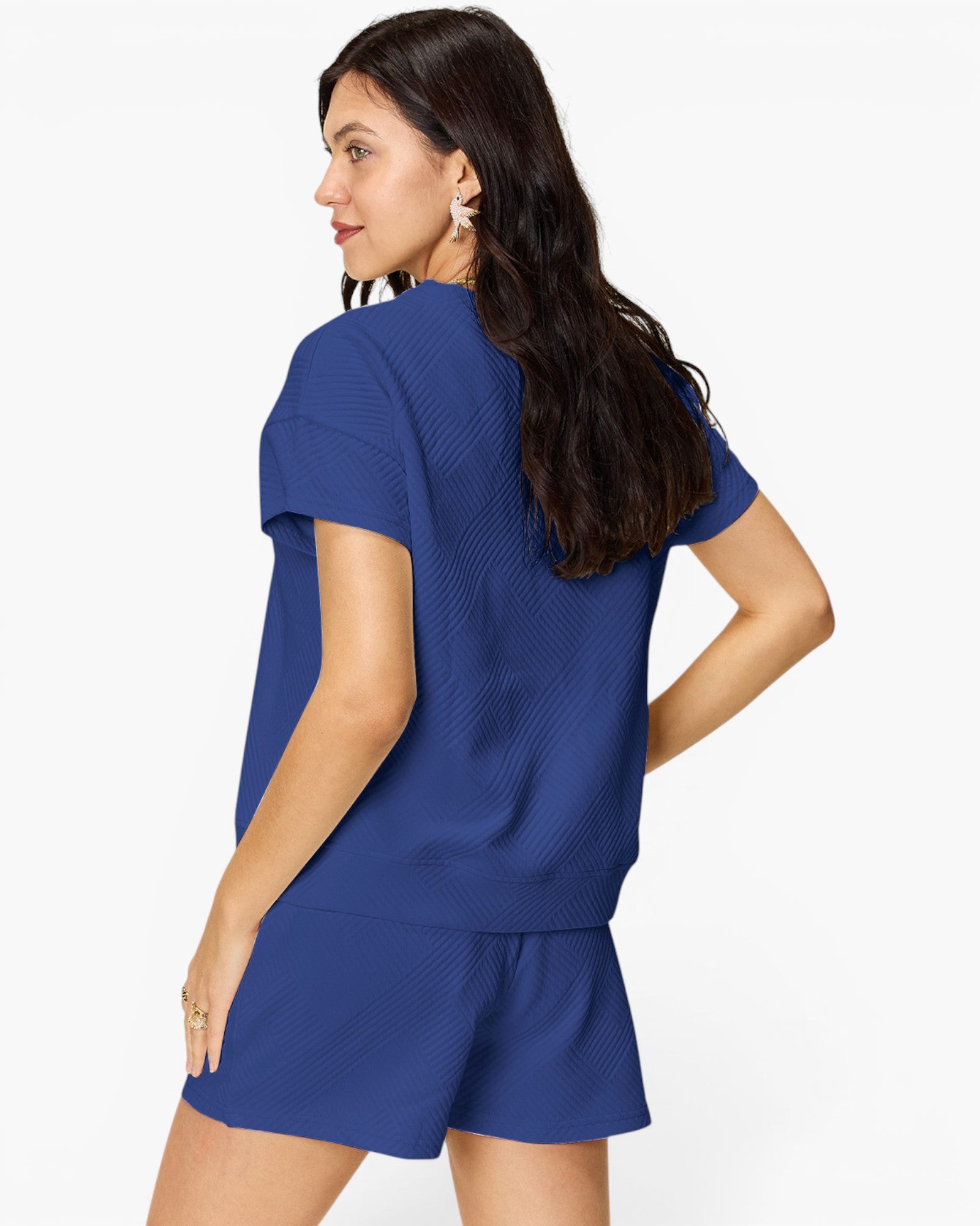 A woman modeling a matching royal blue knit lounge set consisting of a short-sleeve top and shorts, shown from a three-quarters back view against a plain white background.