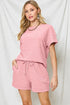 Woman wearing a pink textured outfit with shorts against a white background