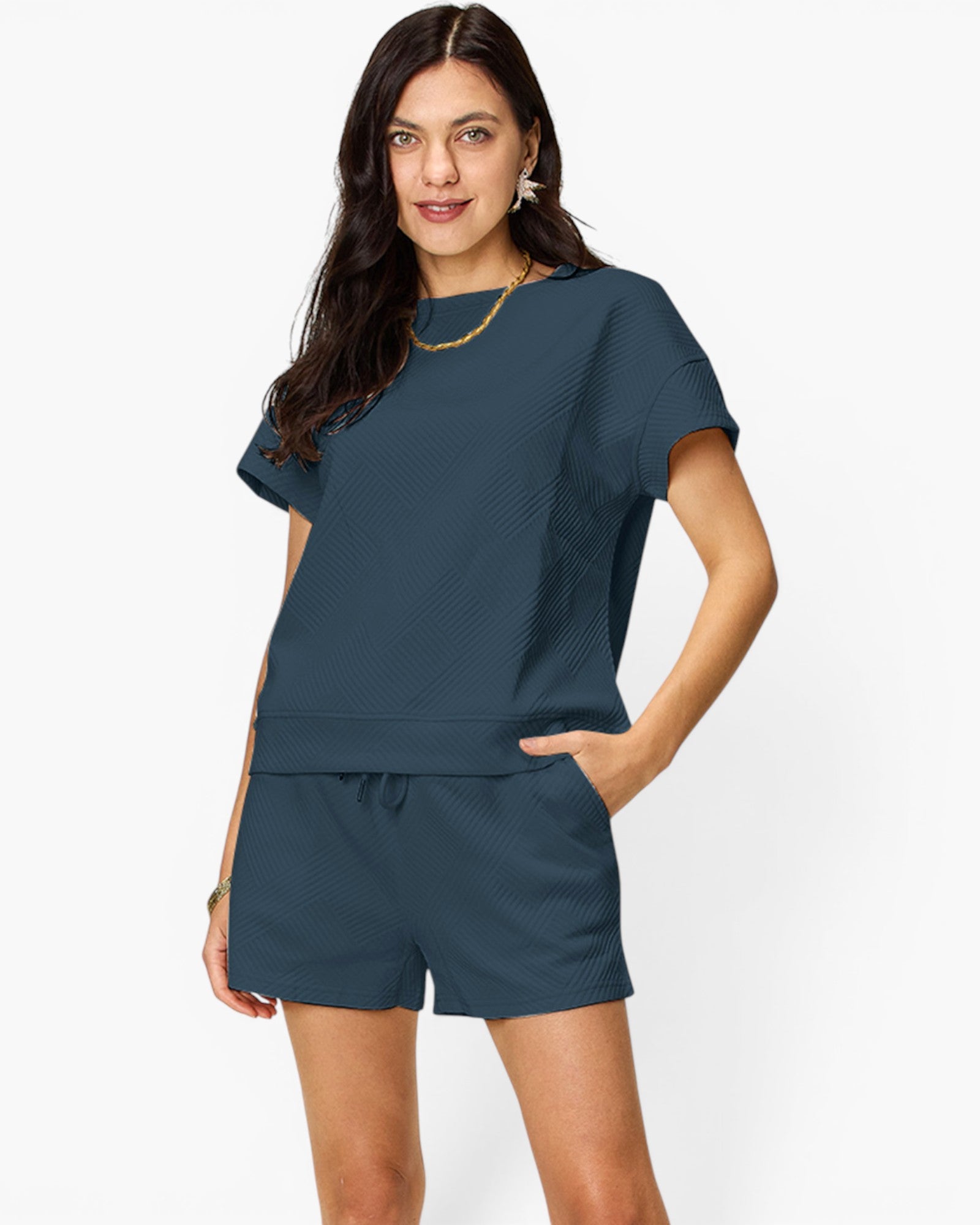 A woman modeling a matching two-piece lounge set consisting of a short-sleeve textured top and coordinating shorts in a muted slate blue color, set against a plain white studio background.