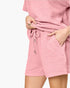 A close-up of a person wearing a textured pink crinkle fabric romper or dress with a drawstring waist and side pockets, shown against a plain light background.