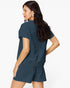 A woman shown from the back wearing a dark slate blue knit short-sleeve top and matching shorts against a plain white background.