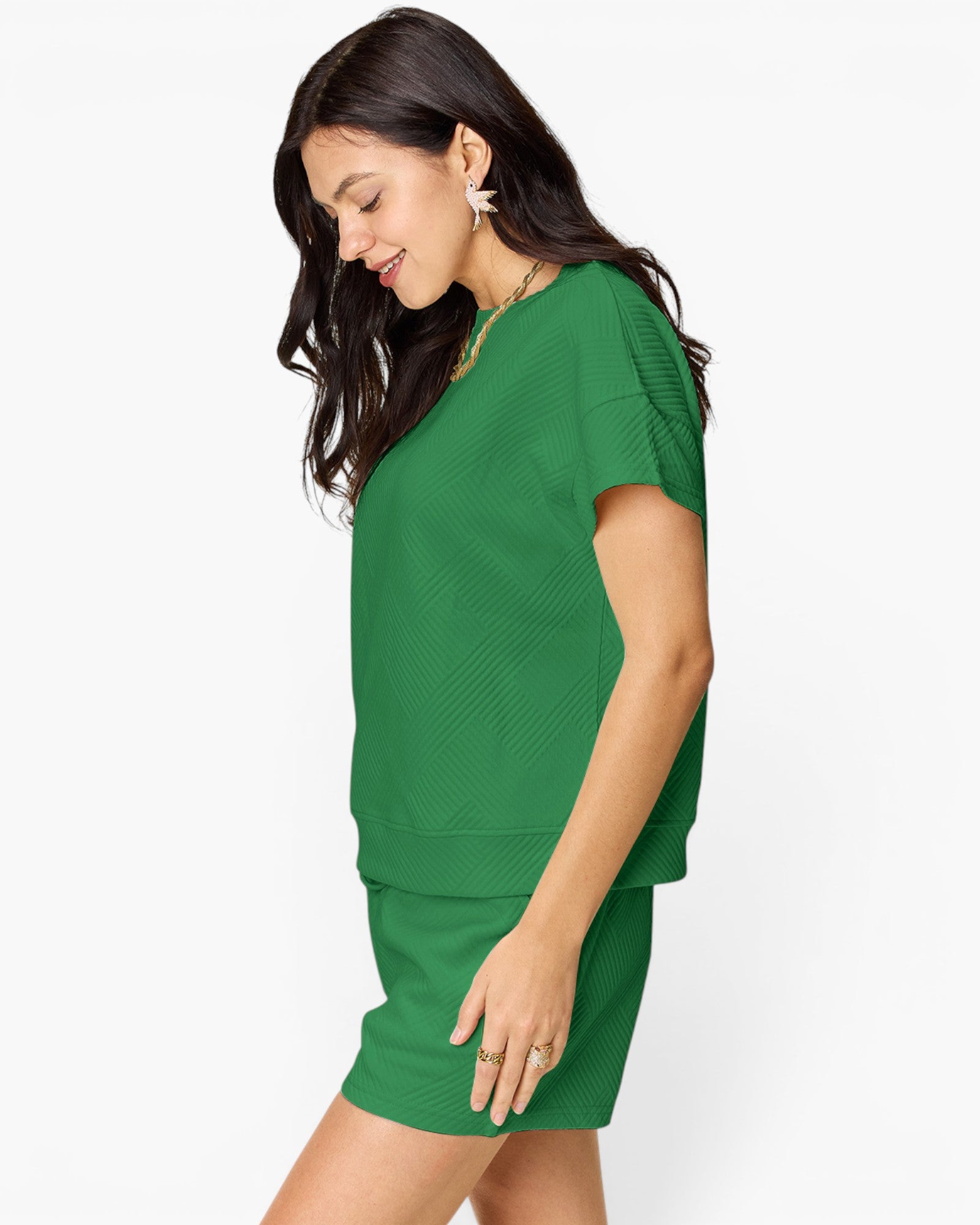 A woman wearing a bright green knit short-sleeve top and matching mini skirt, shown from the side against a plain white studio background.