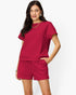 A woman modeling a matching two-piece lounge set in a textured magenta pink fabric, featuring a short-sleeve top and drawstring shorts, against a plain white background.