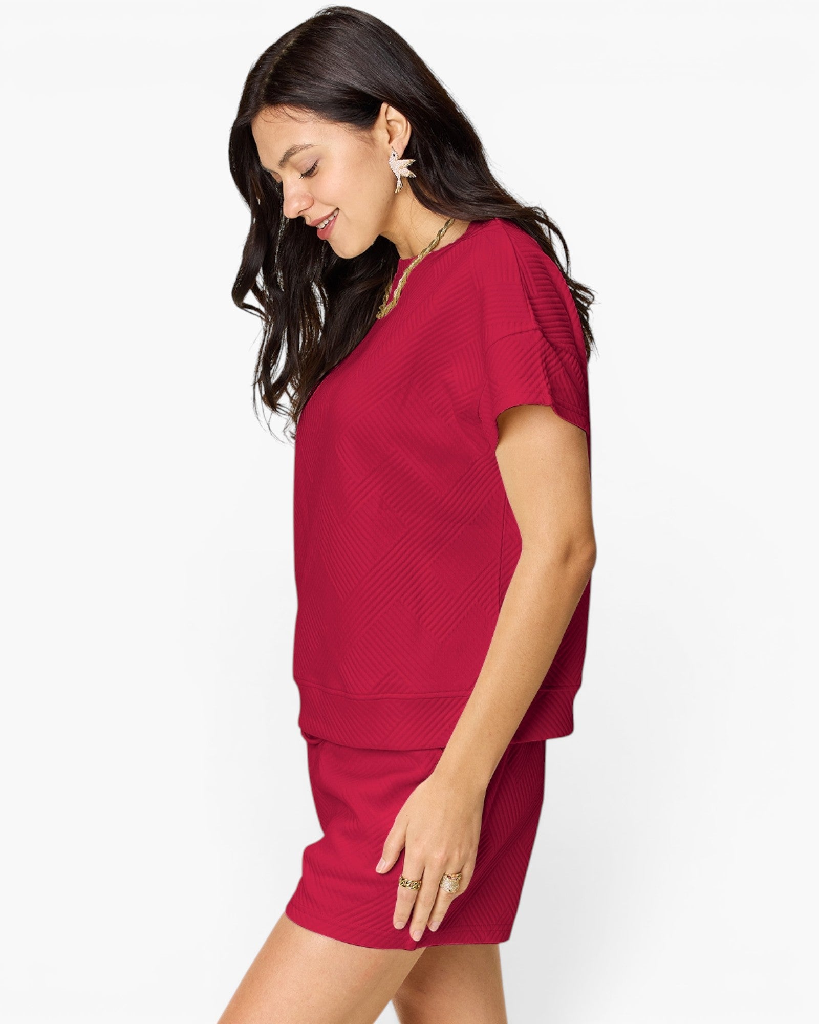 A woman wearing a matching two-piece knit set consisting of a short-sleeve top and a short skirt in a deep red color, shown from a side profile against a plain white background.