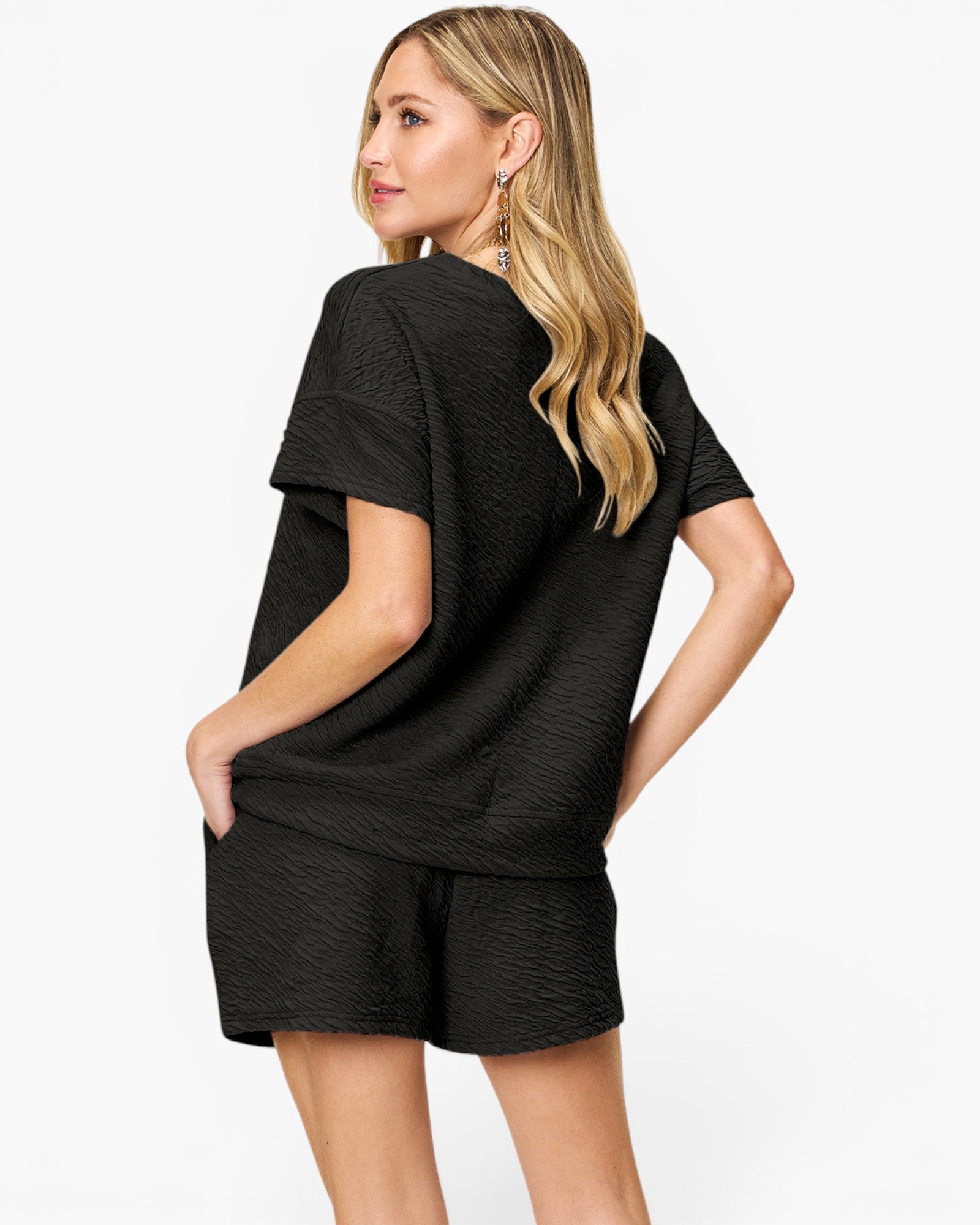 A woman modeling a black textured short-sleeve top and matching shorts against a light gray studio background.