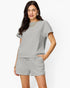 A woman modeling a light gray short-sleeve top and matching shorts set with a subtle textured pattern, photographed against a clean white background.