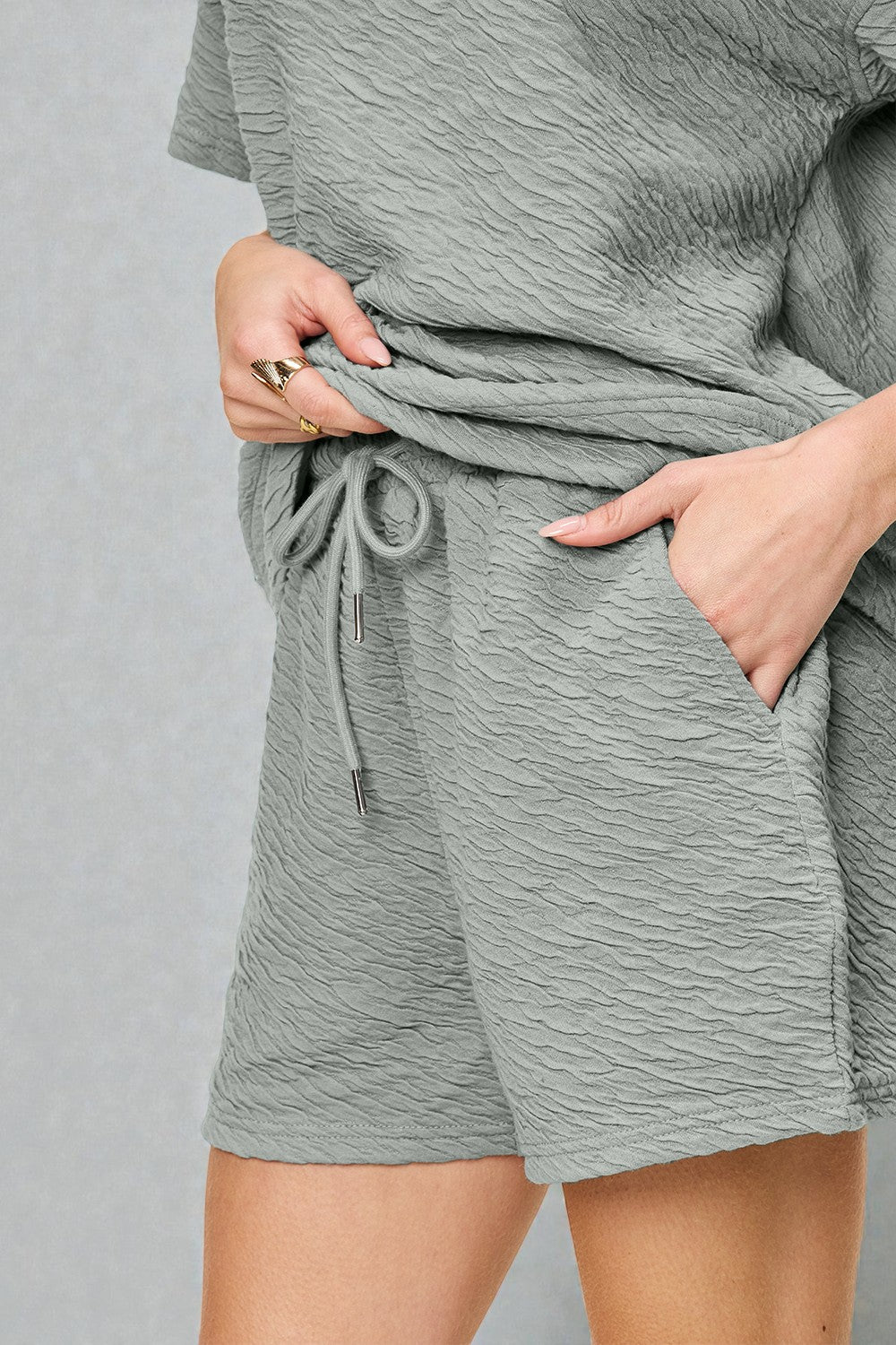 Person wearing a gray textured outfit with shorts and a top on a plain background