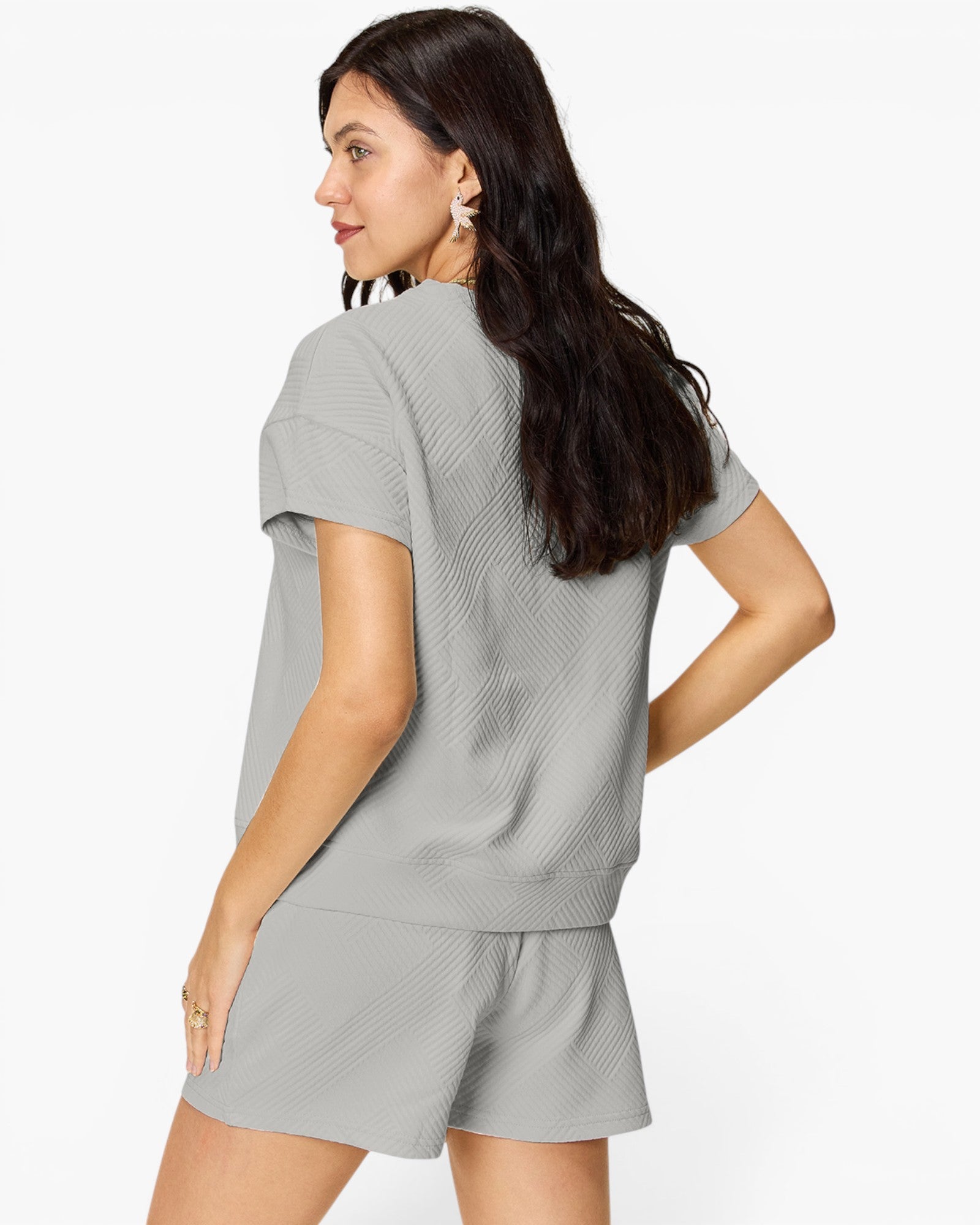 A woman wearing a light gray ribbed knit short-sleeve top and matching shorts, shown from a three-quarters back view against a plain white studio background.