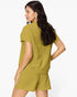 A woman wearing a matching olive green short-sleeve top and shorts set, shown from a three-quarters back view against a plain white studio background.