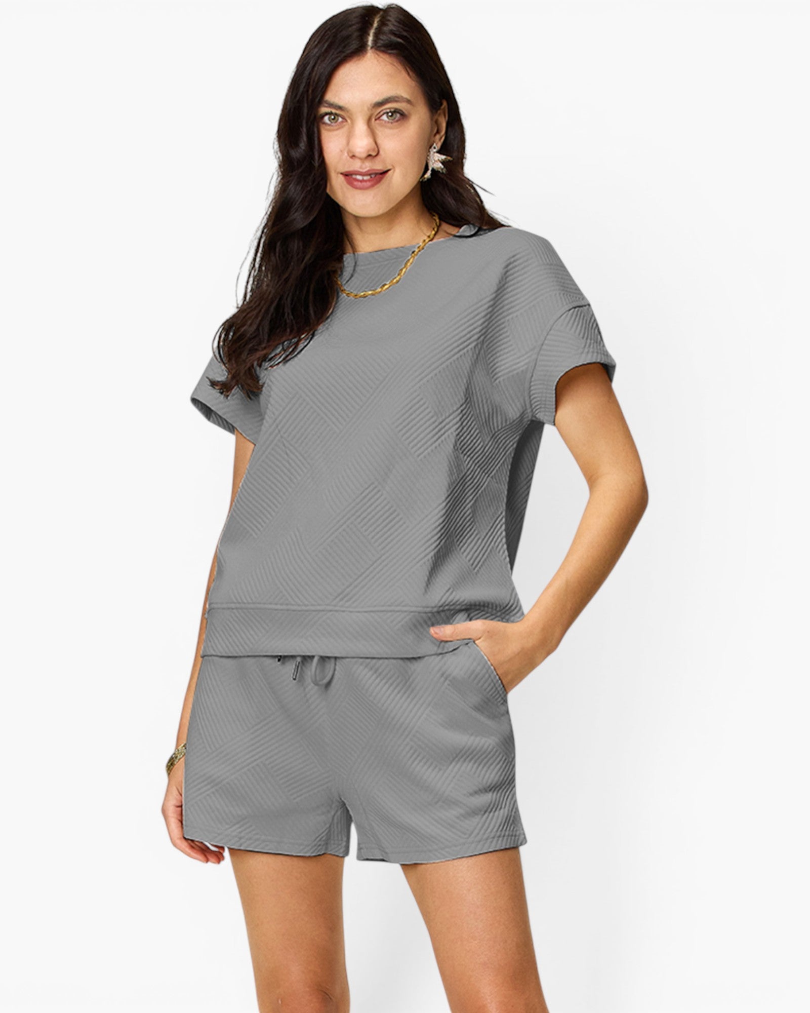 A woman modeling a matching gray short-sleeve top and shorts lounge set with a subtle textured pattern, set against a plain light gray background.