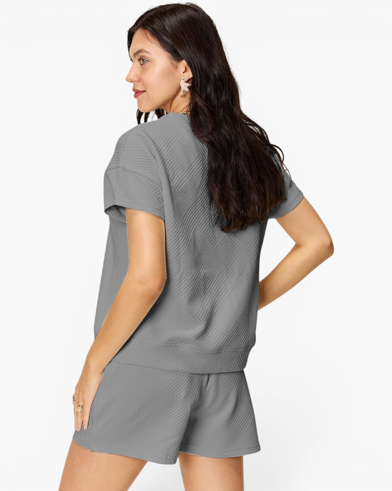 A woman wearing a gray short-sleeve top and matching shorts with a textured waffle pattern, shown from a three-quarters back view against a plain white background.