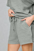 Person wearing a gray textured outfit with shorts and a top on a plain background