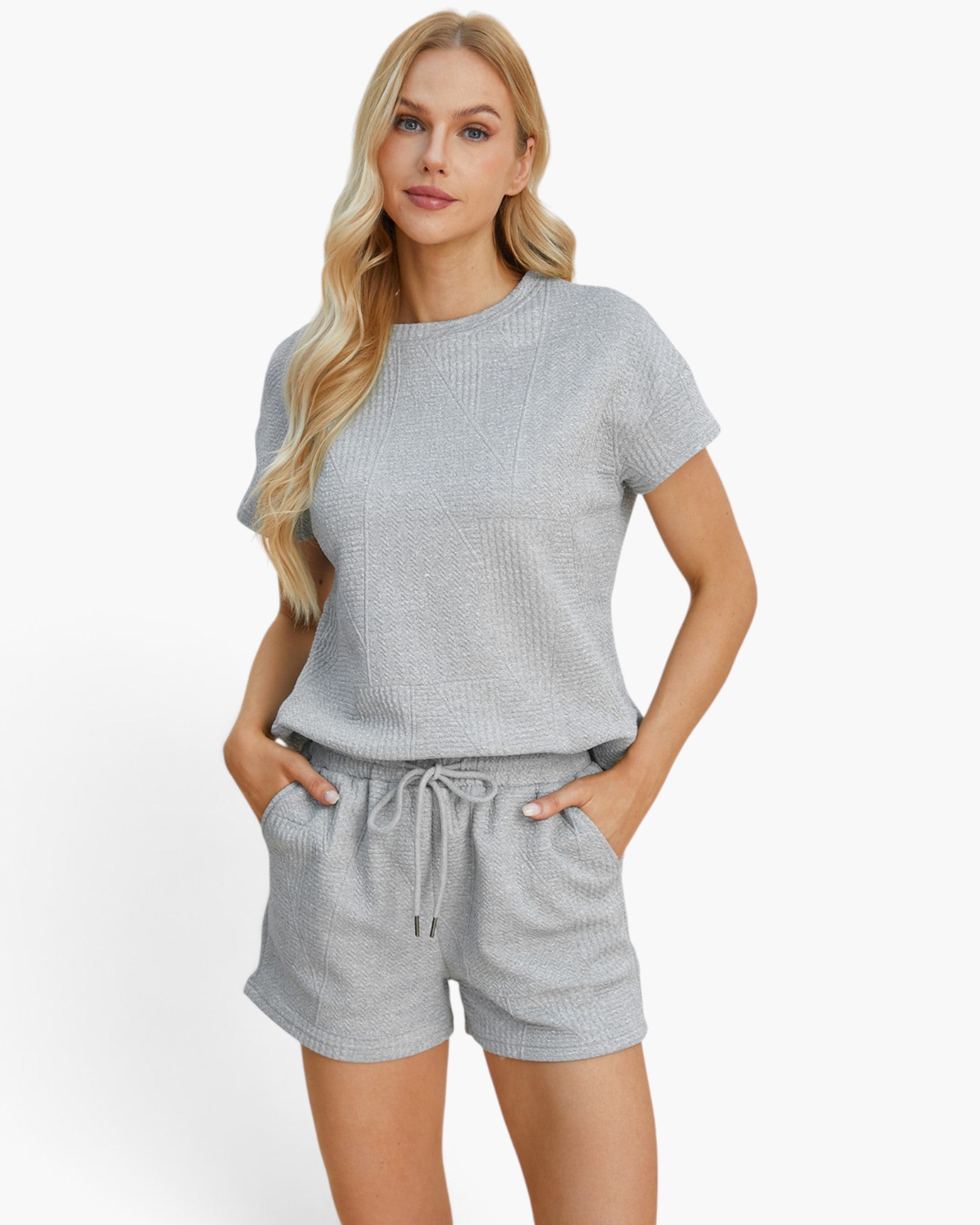 A blonde woman modeling a light gray short-sleeve knit top and matching drawstring shorts against a clean white studio background.