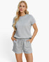 A blonde woman modeling a light gray short-sleeve knit top and matching drawstring shorts against a clean white studio background.