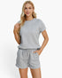 A woman modeling a light gray ribbed knit short-sleeve top and matching gray drawstring shorts against a plain white studio background.