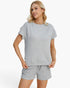 A woman modeling a light gray textured short-sleeve top and matching shorts against a clean white background.