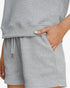 Close-up of a person wearing light gray textured shorts with a drawstring waist and side pocket, with a hand inserted into the pocket.