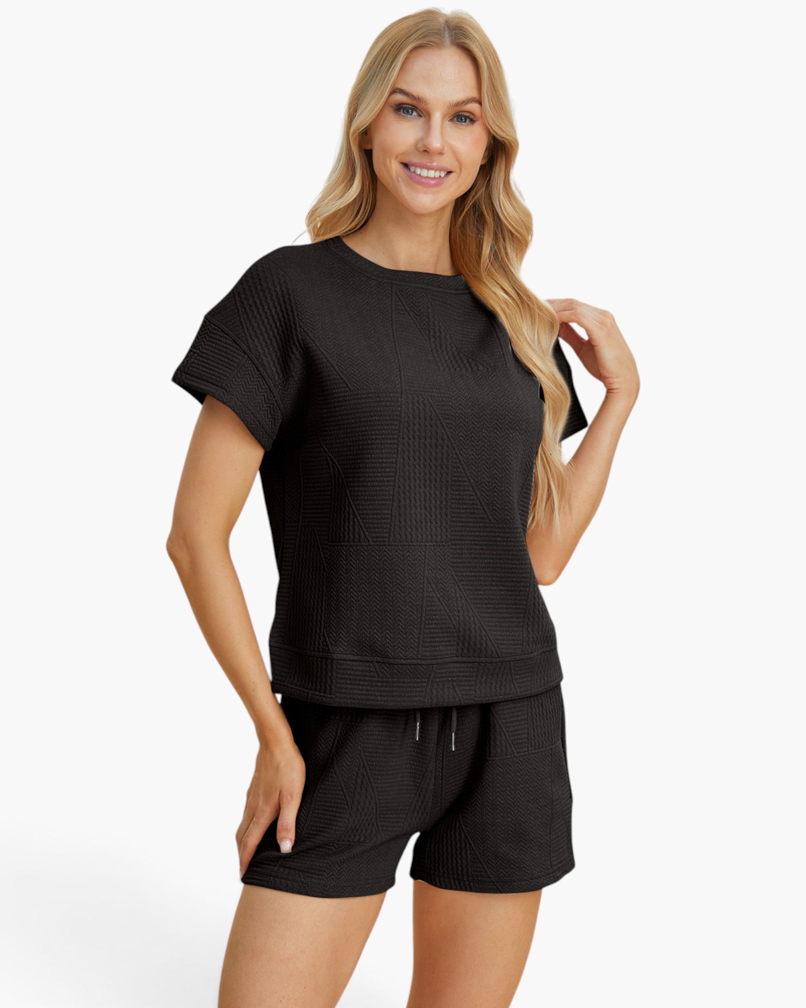 A woman modeling a matching black short-sleeve top and shorts set with a textured waffle-weave pattern, photographed against a clean white studio background.