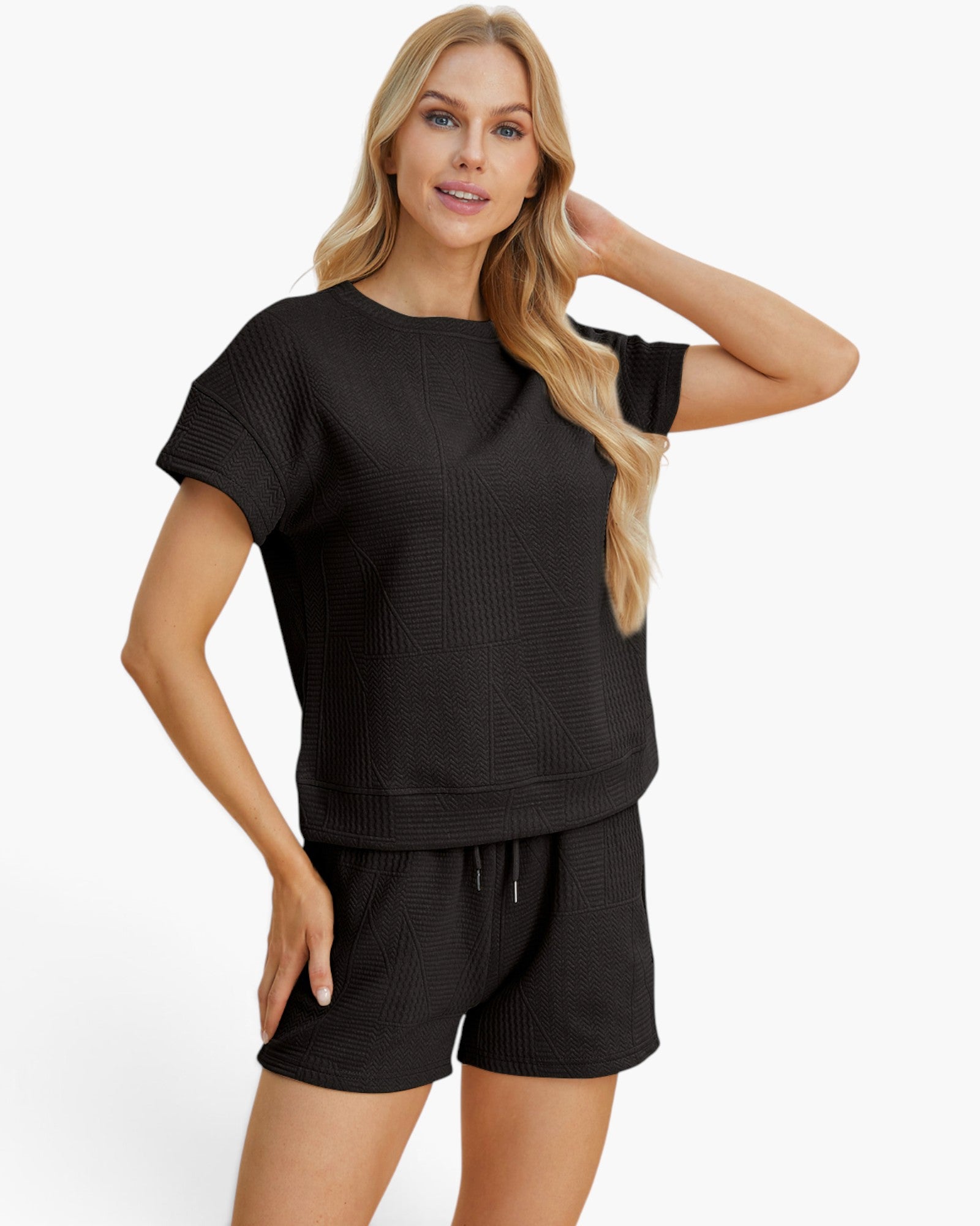 A woman modeling a matching black short-sleeve top and shorts set with a textured waffle-weave pattern, photographed against a clean white studio background.
