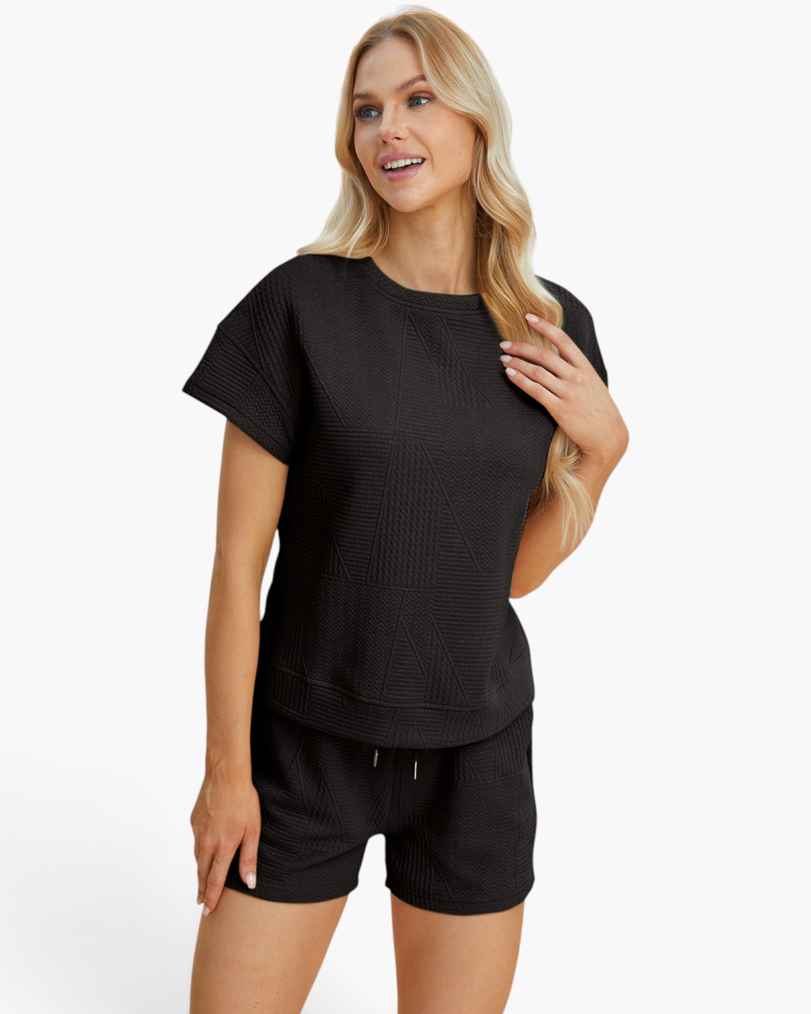 A blonde woman modeling a black short-sleeve textured top and matching black shorts against a plain white studio background.