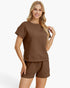 A woman modeling a matching brown short-sleeve top and shorts set with a textured waffle-weave pattern, photographed against a clean white background.