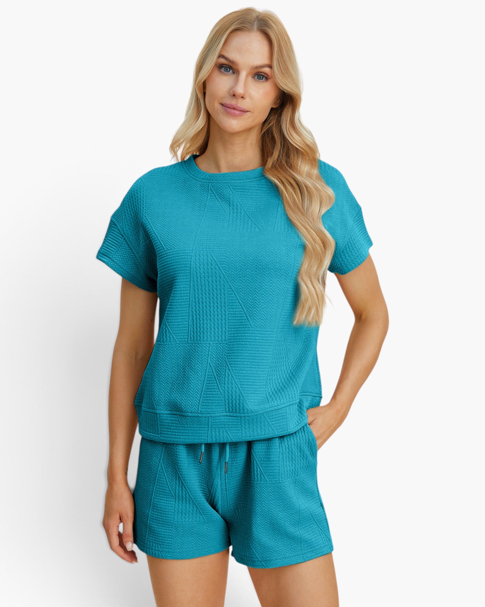 A woman modeling a matching turquoise blue lounge set consisting of a short-sleeve textured top and coordinating shorts against a plain white studio background.