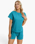 A blonde woman modeling a matching teal short-sleeve knit top and shorts set against a clean white studio background.