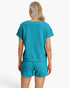 A woman shown from the back wearing a matching turquoise short-sleeve top and shorts set with a textured geometric pattern, against a plain white studio background.