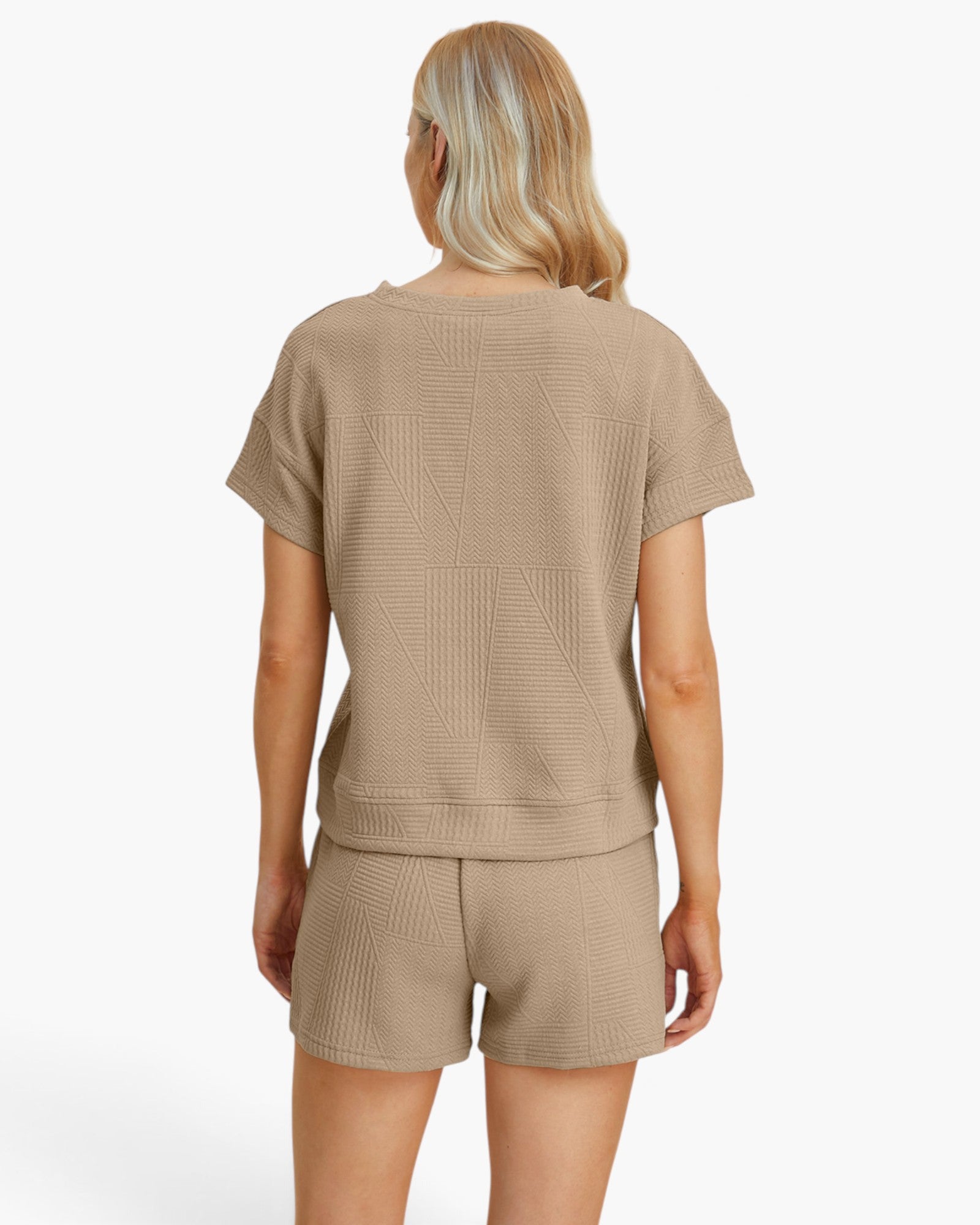 A woman shown from the back wearing a beige short-sleeve cropped top and matching shorts with a textured geometric pattern, set against a plain white studio background.