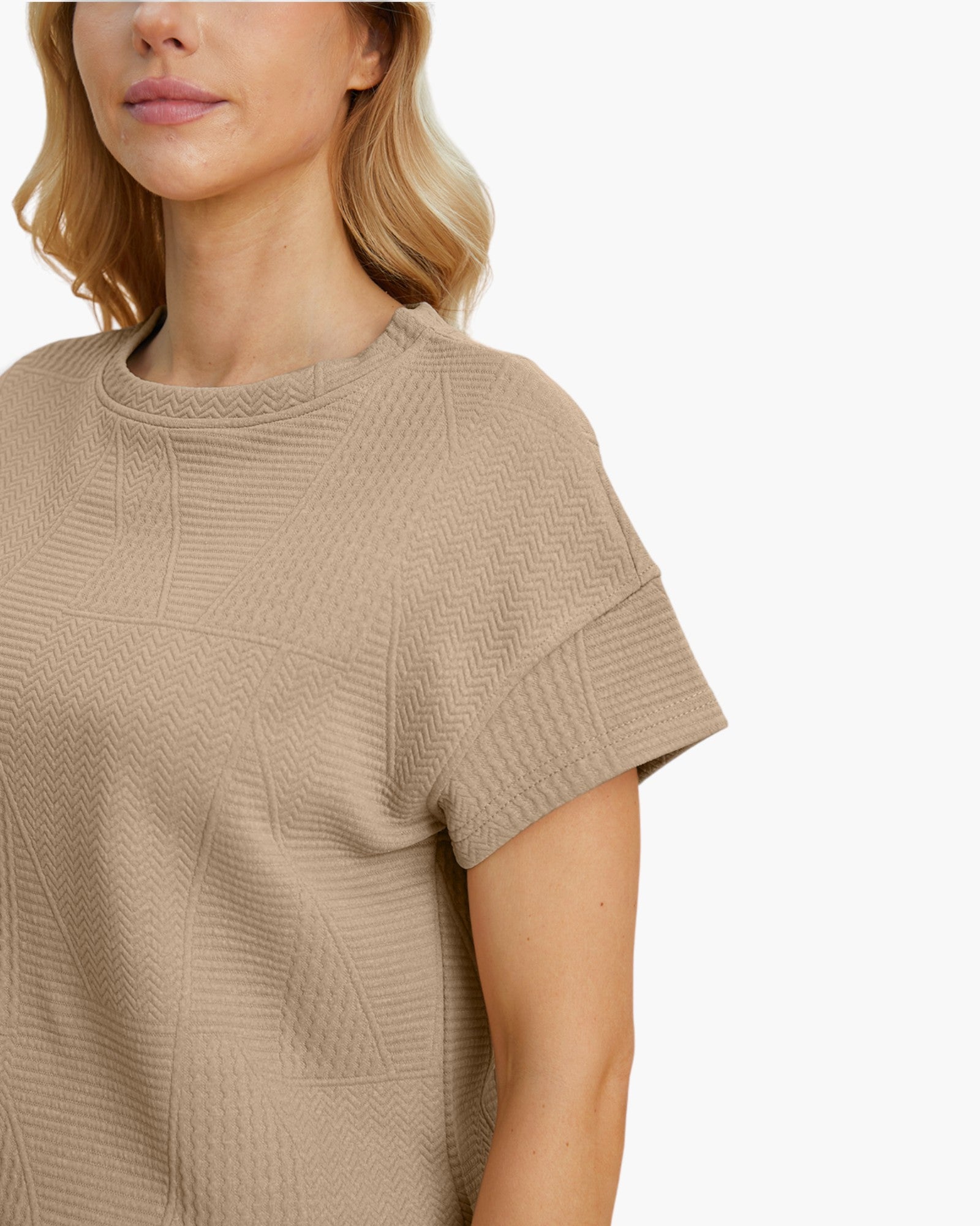 Close-up of a woman wearing a beige short-sleeve textured knit top against a plain white background.