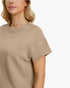 Close-up of a woman wearing a beige short-sleeve textured knit top against a plain white background.