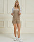 Woman wearing beige overalls against a light-colored wall.