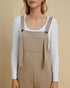 Person wearing beige overalls with a white long-sleeve shirt on a beige background