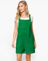 A woman modeling a bright green textured overall romper with shoulder straps and a white short-sleeve t-shirt underneath, photographed against a clean white studio background.