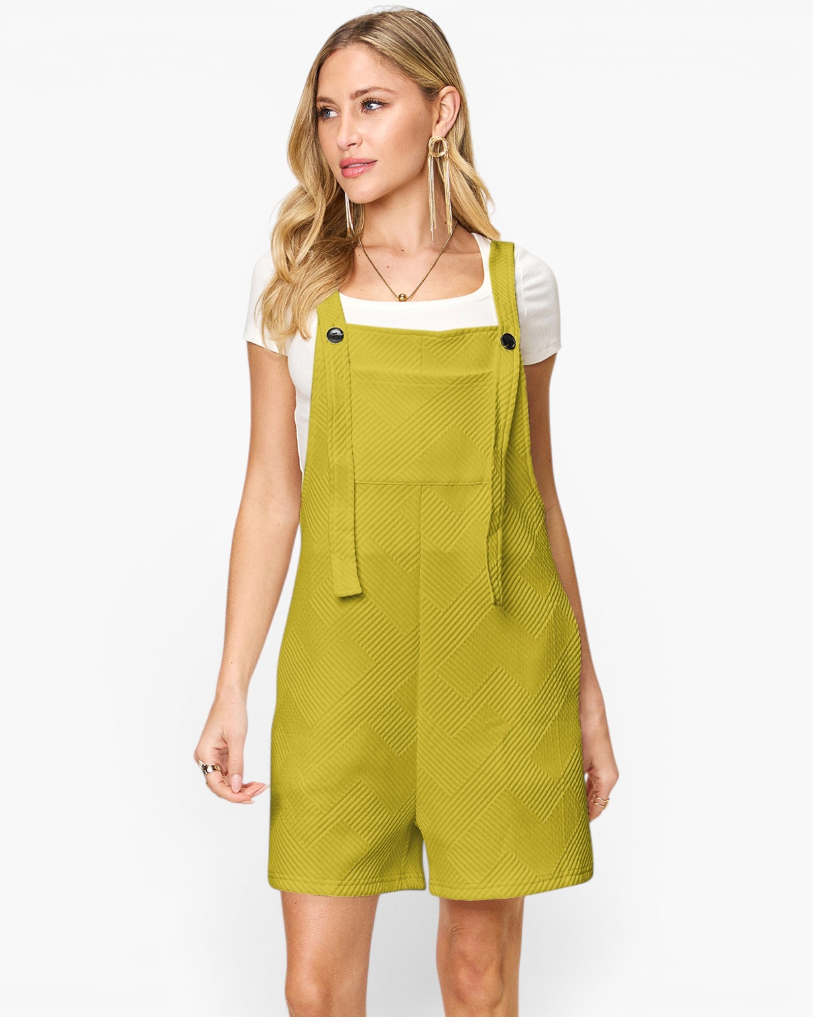 A woman modeling a bright yellow-green overall romper with a textured pattern, worn over a white t-shirt, against a plain white background.