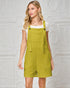 Woman wearing a green quilted overalls dress against a decorative white wall.