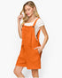 A woman modeling a bright orange textured overall jumpsuit over a white short-sleeve t-shirt, set against a plain light gray studio background.