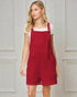 Woman wearing a red pinafore dress against a gray paneled wall