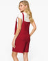 A woman modeling a red textured pinafore-style dress over a white short-sleeve top, shown from the back against a plain light background.
