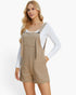 A woman modeling a pair of beige textured overall shorts with a white long-sleeve top underneath, set against a plain white studio background.