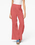 A model wearing a pair of wide-leg, high-waisted pants in a dusty rose or coral pink color, paired with a white top and blue platform sandals, against a plain white studio background.